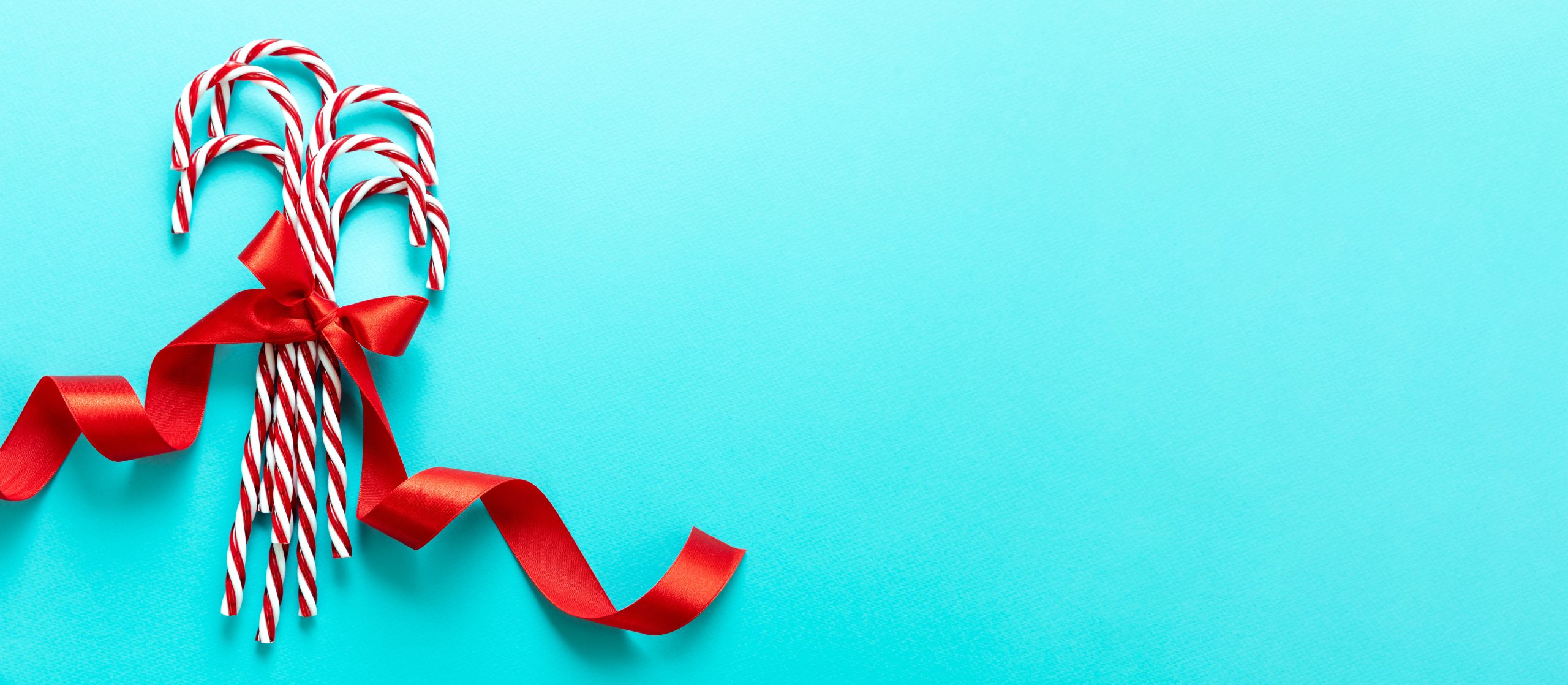 Candy canes bunch on blue background. Christmas peppermint red white candies with red ribbon bow. Merry Xmas greeting card template, copy space